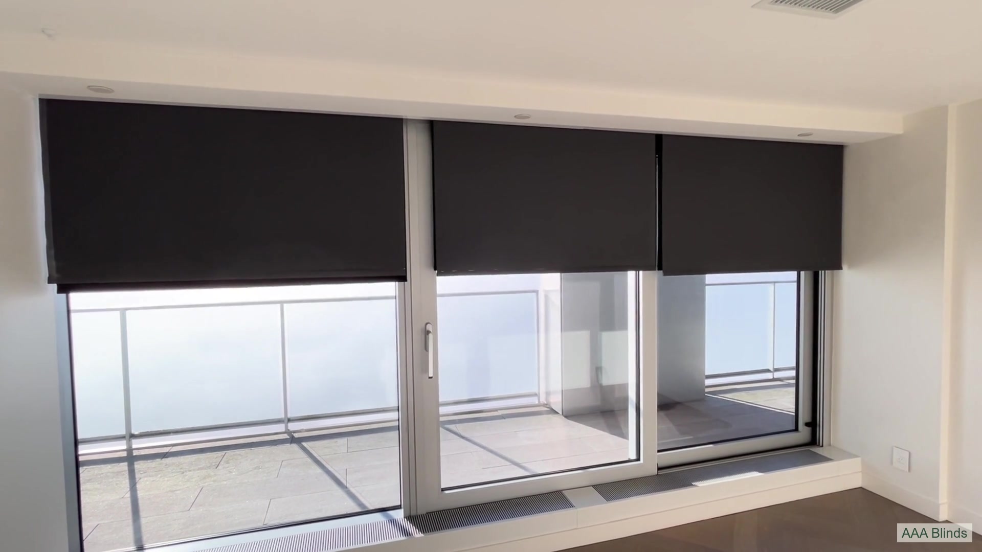Motorized roller shades rising above a high-rise balcony with a cloud-filled sky beyond