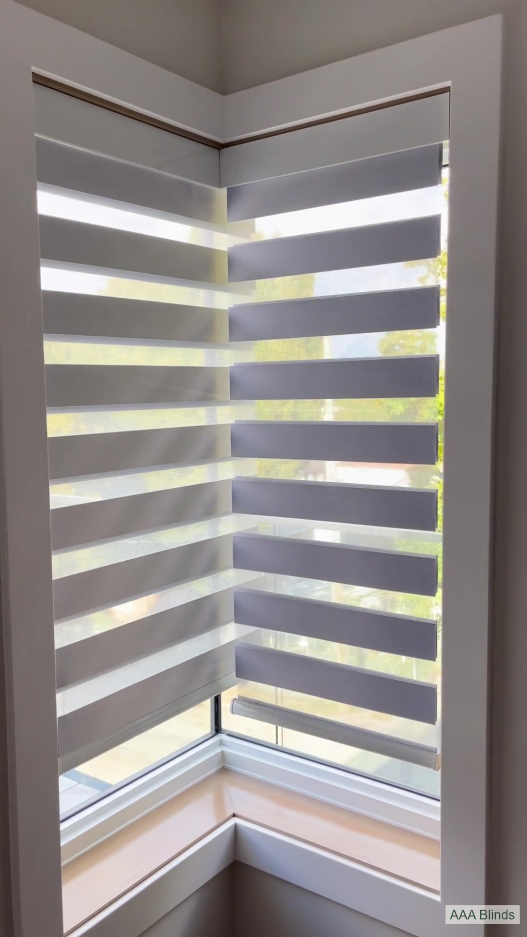Two motorized zebra shades overlap at a right-angle glass corner