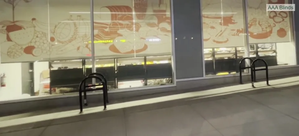 Printed roller shades lowered across storefront windows, with AAA Blinds signature