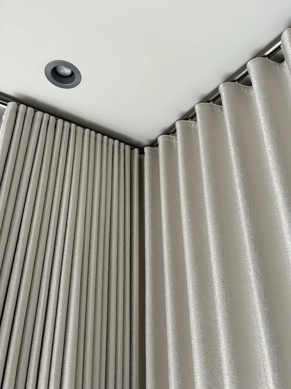 A close view of textured curtain fabric, evenly spaced folds and tracks meeting at a ceiling corner