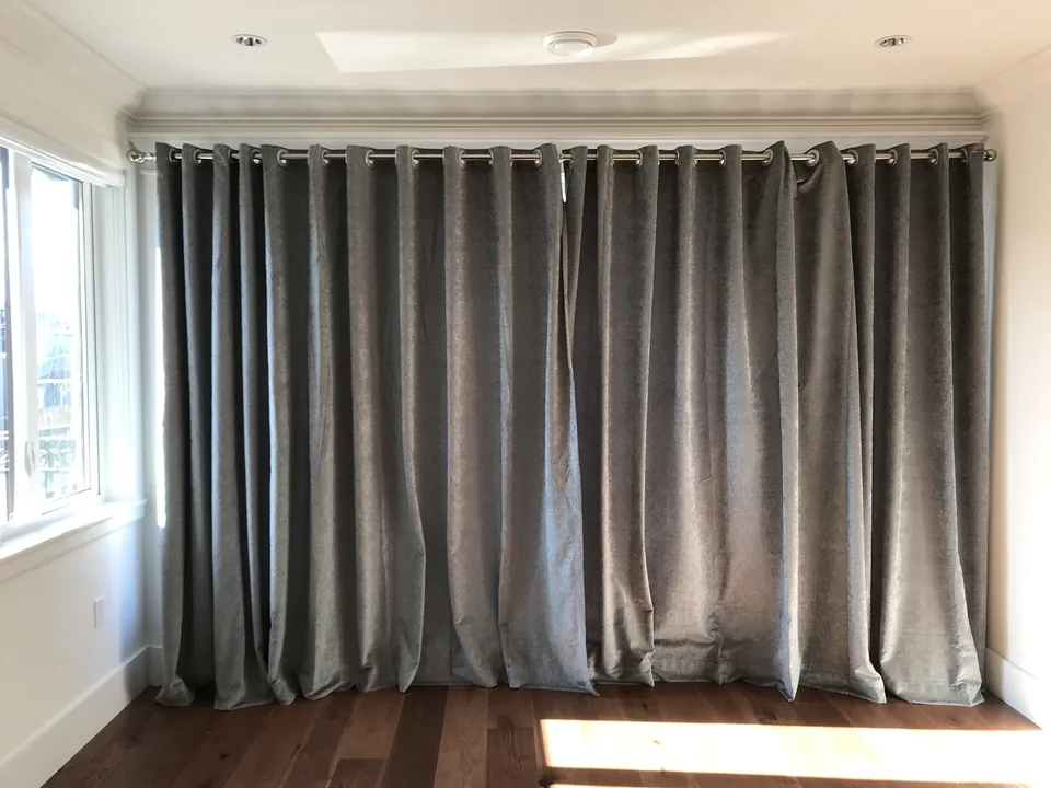 Grey drapery hangs from a dark pole through a row of eyelets