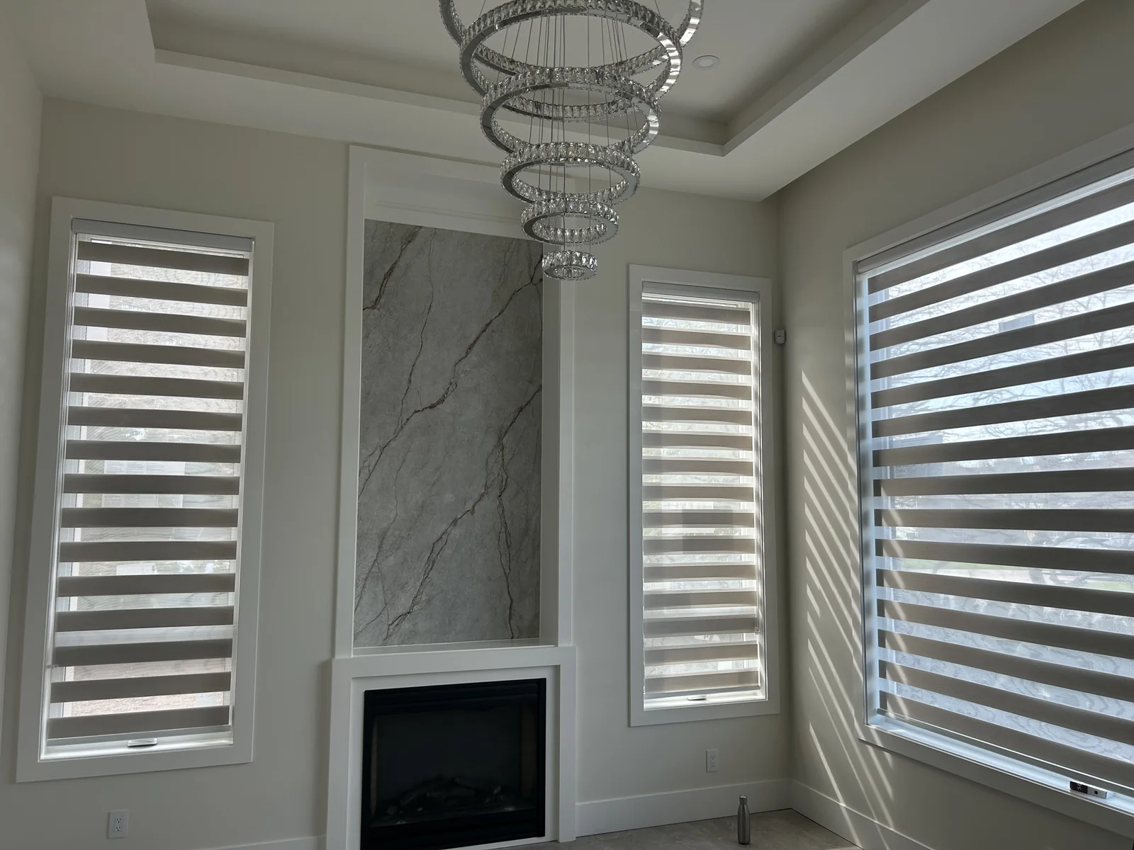 Matching zebra shades at two narrow windows beside a marble fireplace and a wider adjacent window