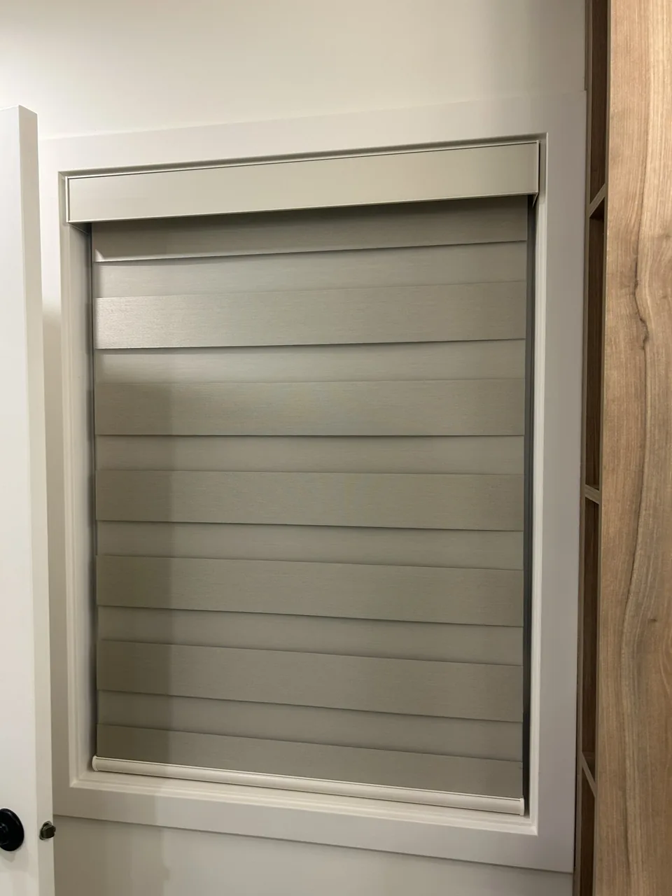 A close view of a dual shade in a narrow framed opening, with its fabric bands aligned and a matching headrail above