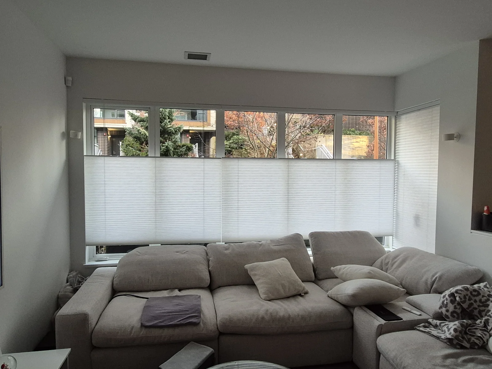 White top-down cellular shades across corner windows behind a sectional sofa