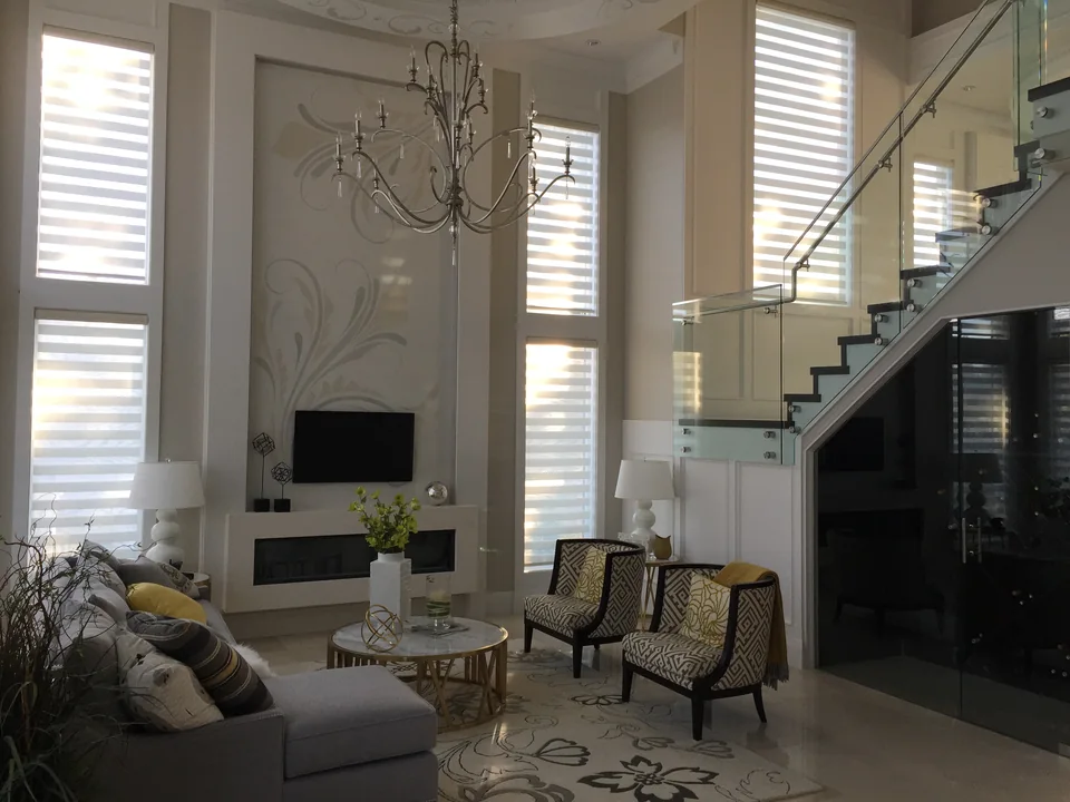 Motorized dual shades follow two levels of windows beside a glass staircase