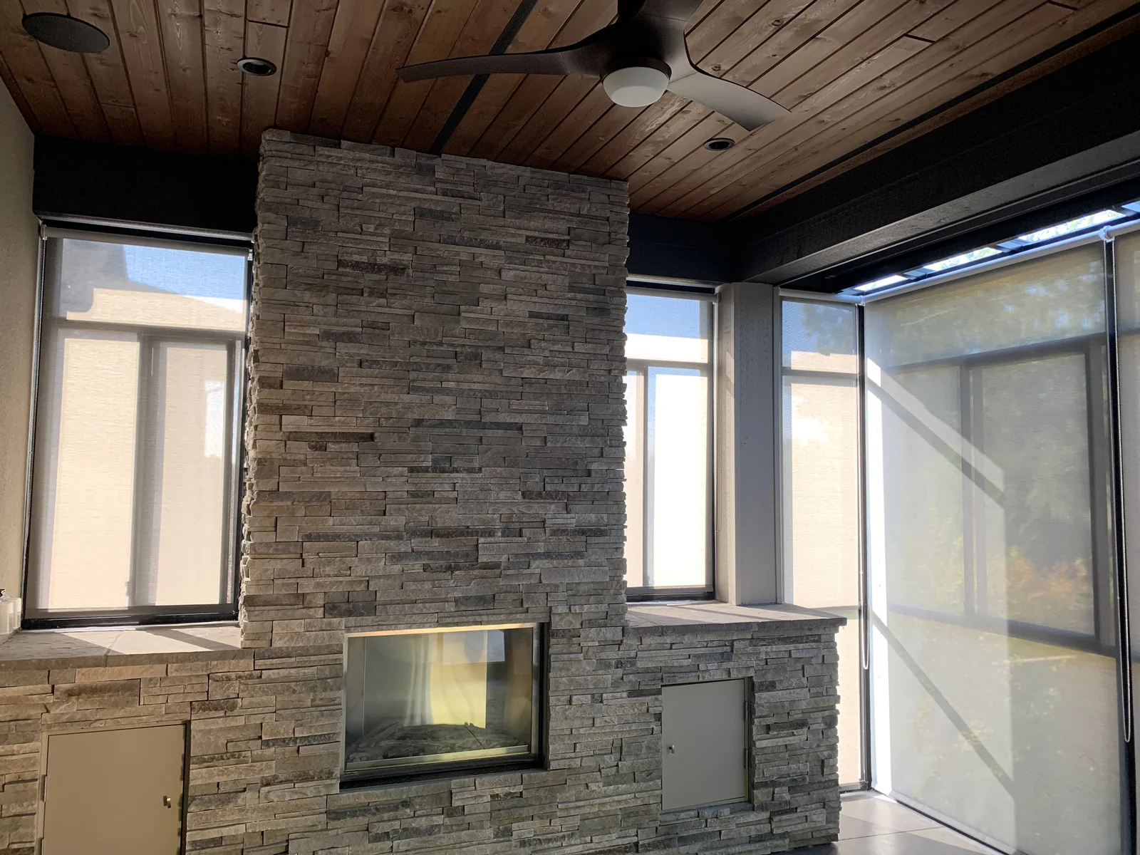 Roller shades at the glazing around a stone fireplace in a covered patio room