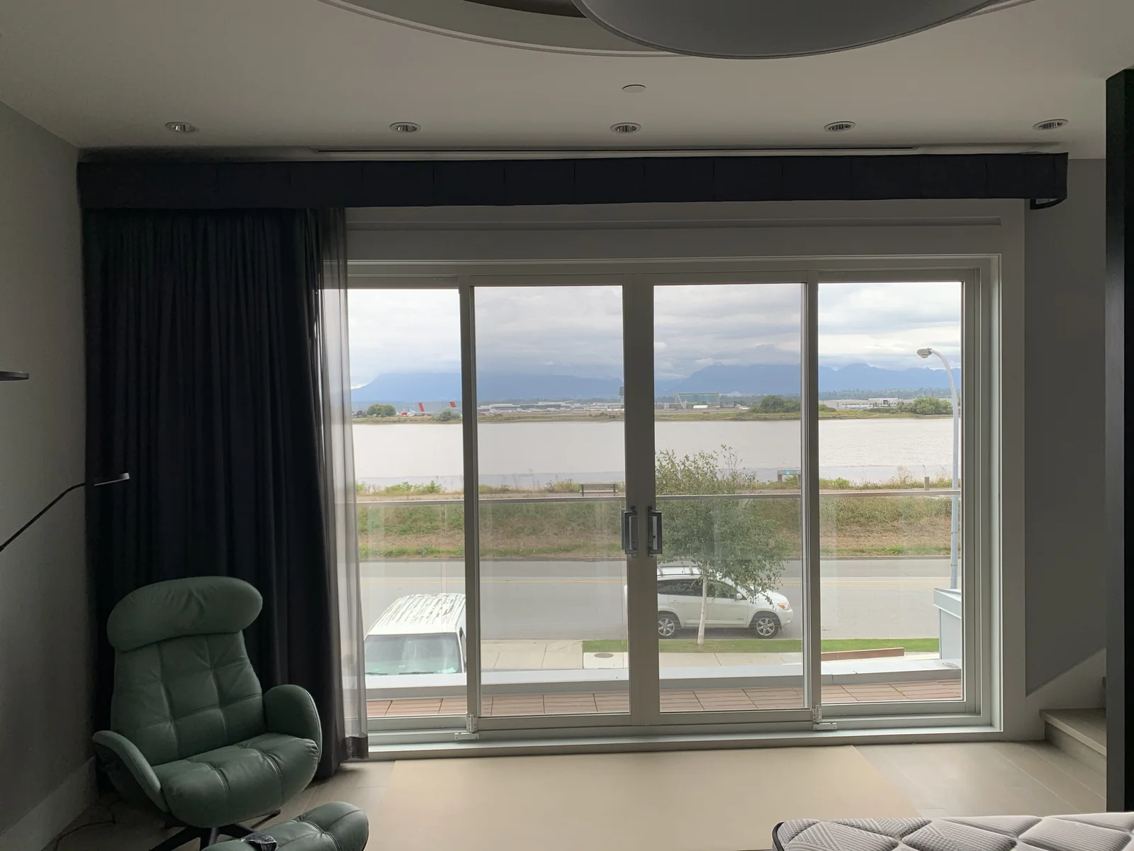 Sheer curtain drawn to the side of a wide window beside dark drapery and a green chair