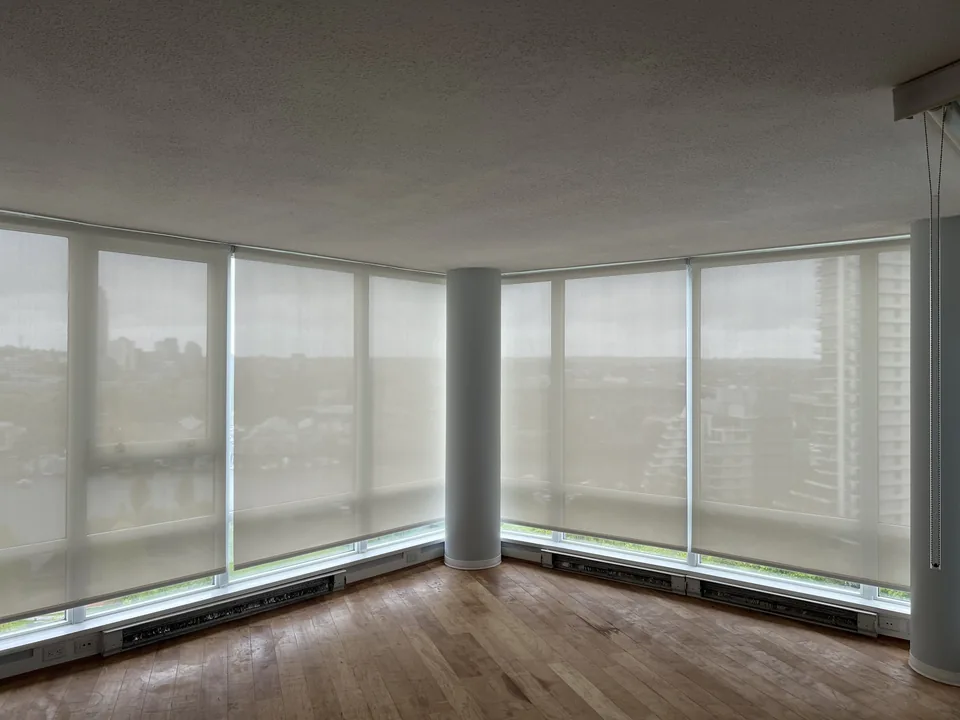 Pale roller-shade panels follow a corner of tall glazing