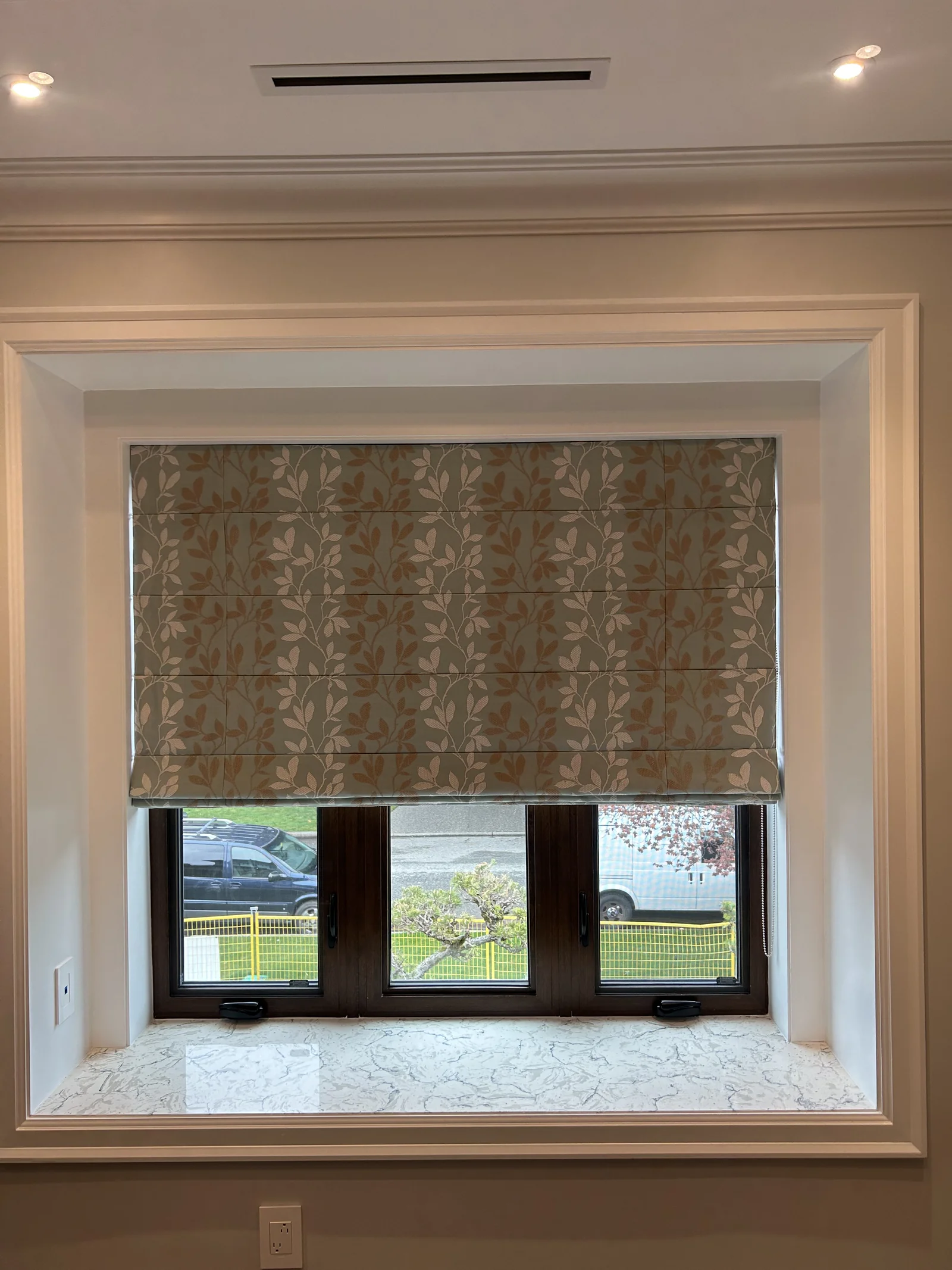 Botanical patterned Roman shade lowered across a dark framed window above a marble sill
