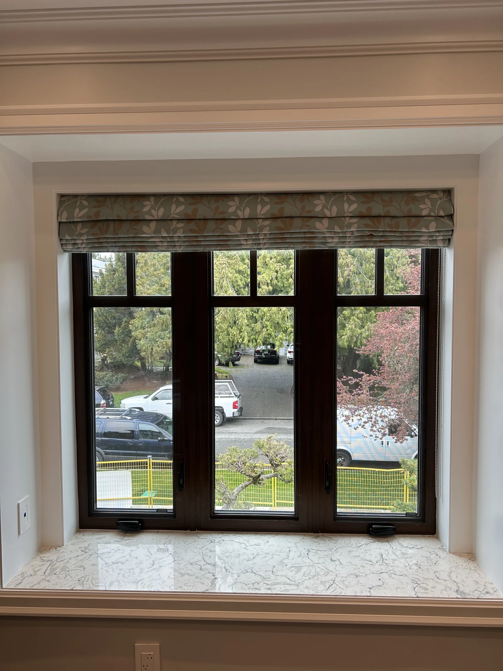 The same botanical patterned Roman shade raised into horizontal folds above a dark framed window and marble sill