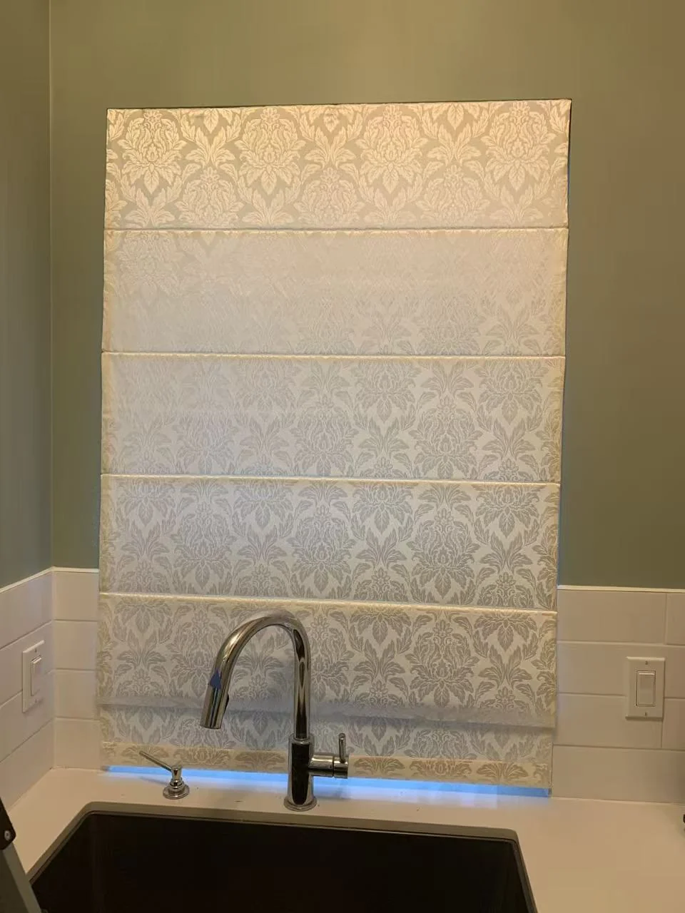 A pale patterned Roman shade with horizontal fabric folds above a bathroom basin