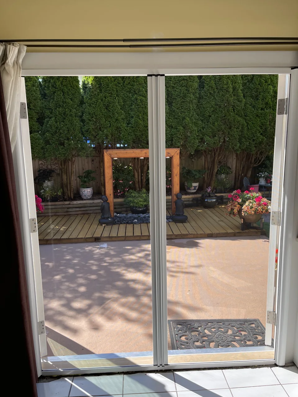White centre-meeting retractable screens across a garden doorway with flowers and a green hedge beyond