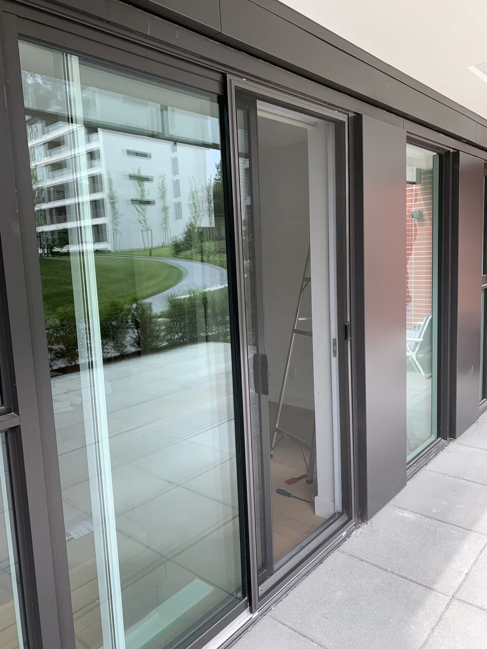 Charcoal-framed sliding mesh screen door beside patio glazing, with its handle and bottom track visible