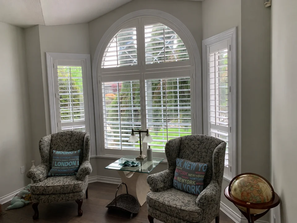 White shutter panels following a tall arched window between two sitting-room chairs