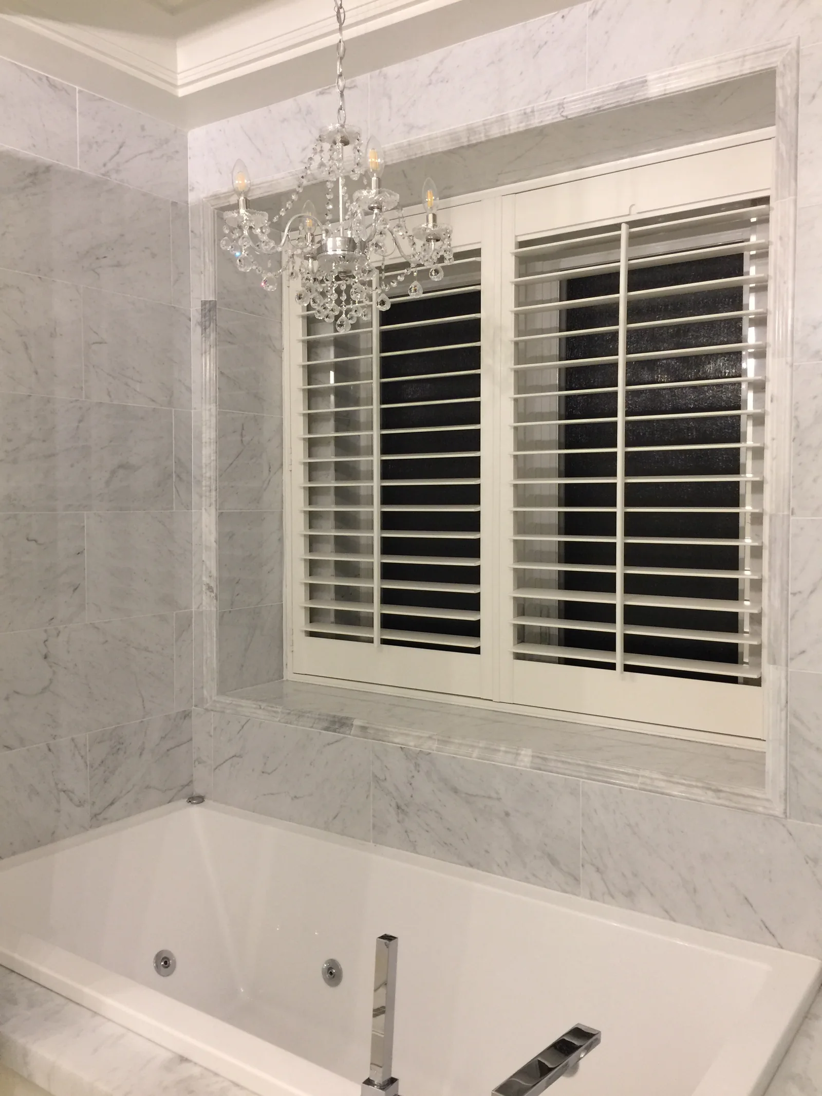 White shutters above a bathtub, framed by marble-patterned walls