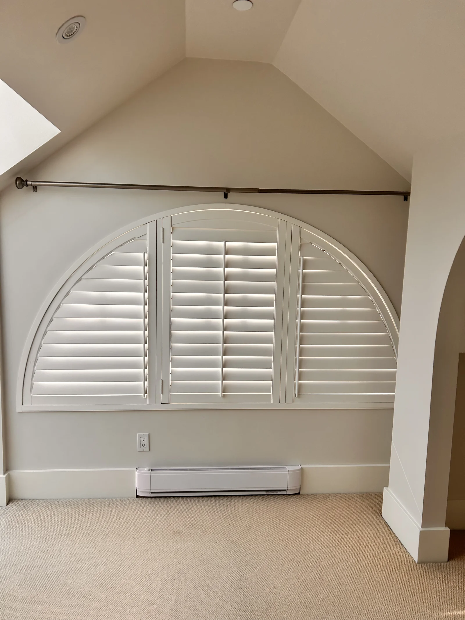 White shutter panels and a curved frame fitted to a half-round window beneath a sloping ceiling