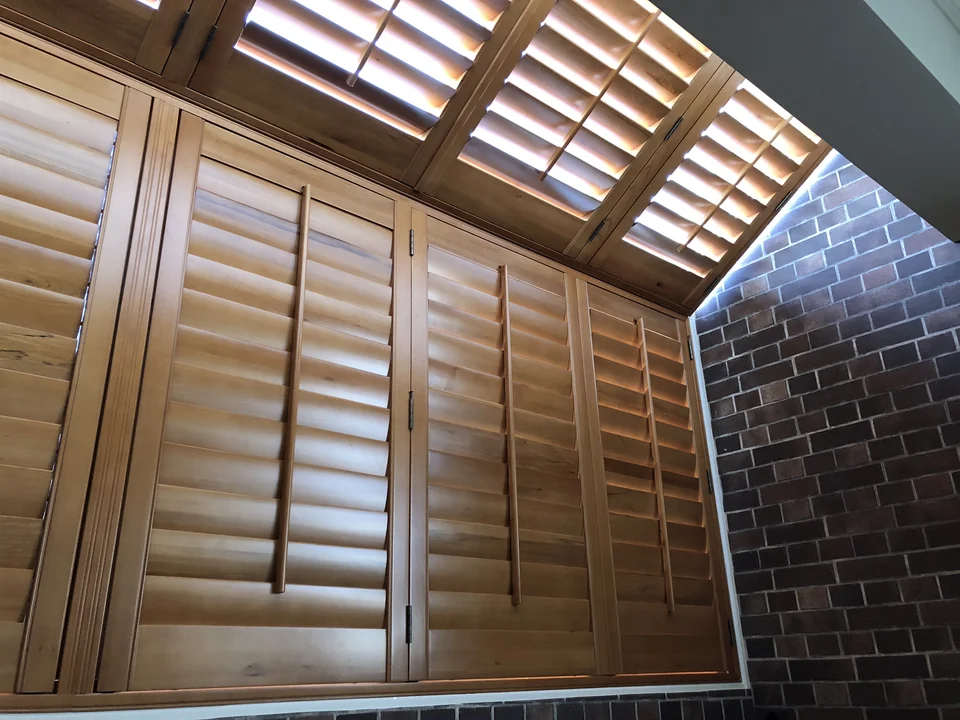 Warm wood-toned shutter panels continue from the wall onto the sloping skylight, bringing a coordinated finish to the glazed corner