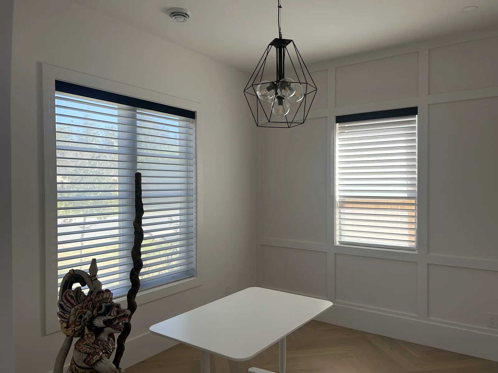 White Vienna shades at two corner windows, with a geometric pendant and trees visible through the sheer fabric