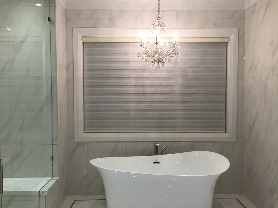 Two coordinated dual shades above a freestanding bathtub, with the fabric bands aligned