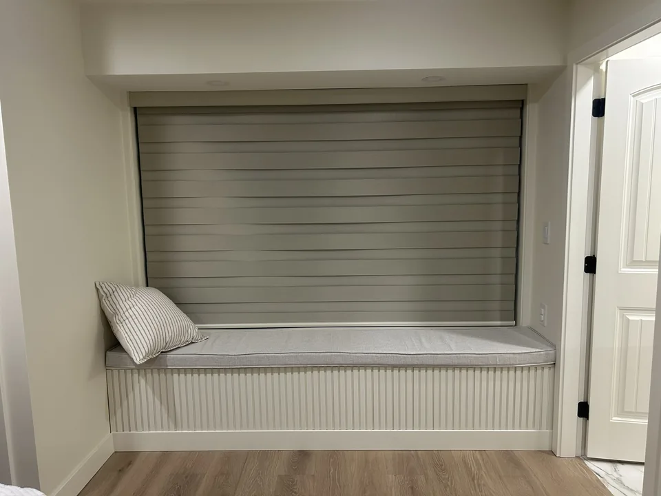 A layered zebra shade sits within a deep window opening above a built-in seat